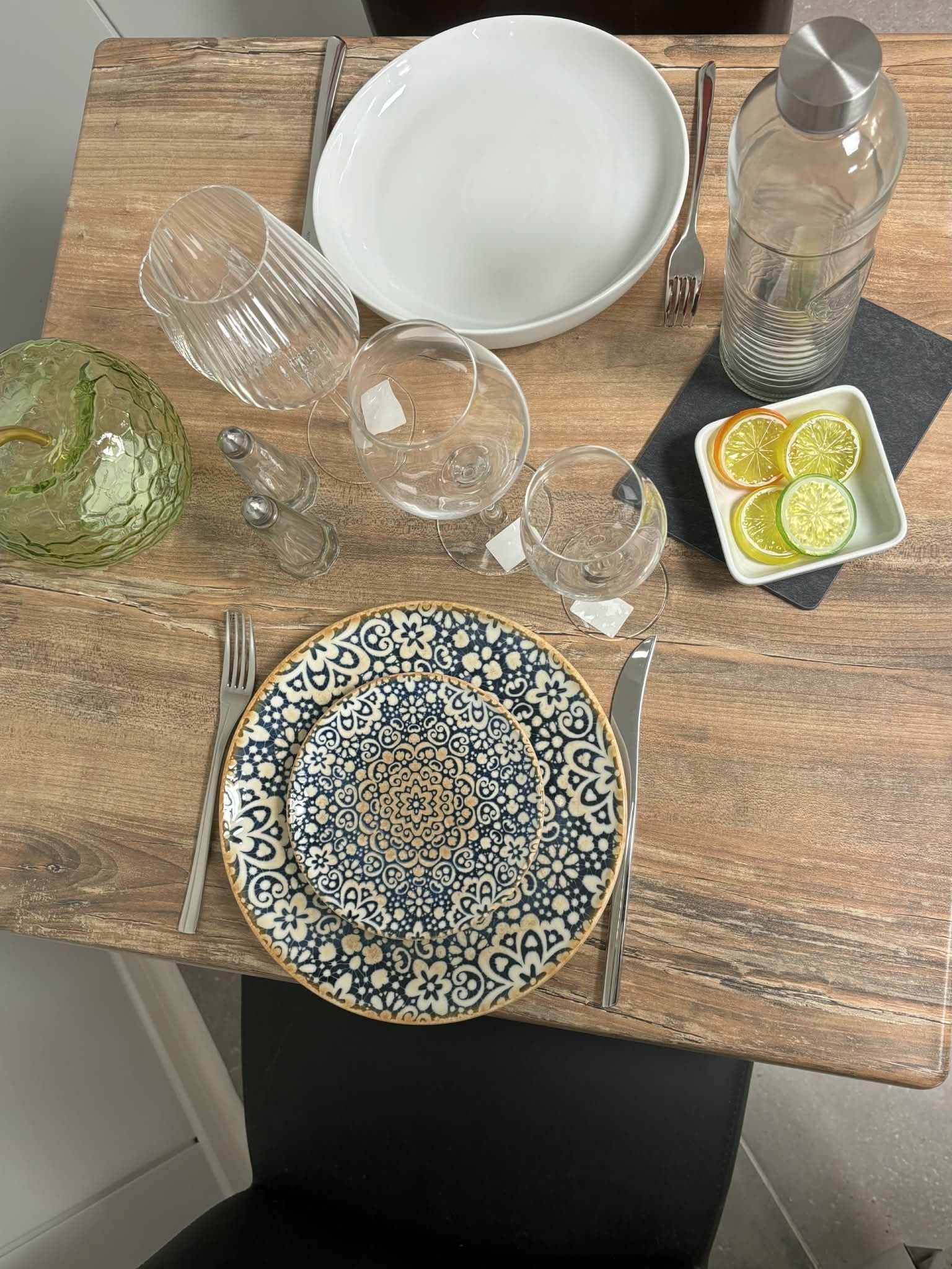 Table dressée avec assiettes, verres et une gourde en verre ; comprend des tranches de citron vert et un bol décoratif.