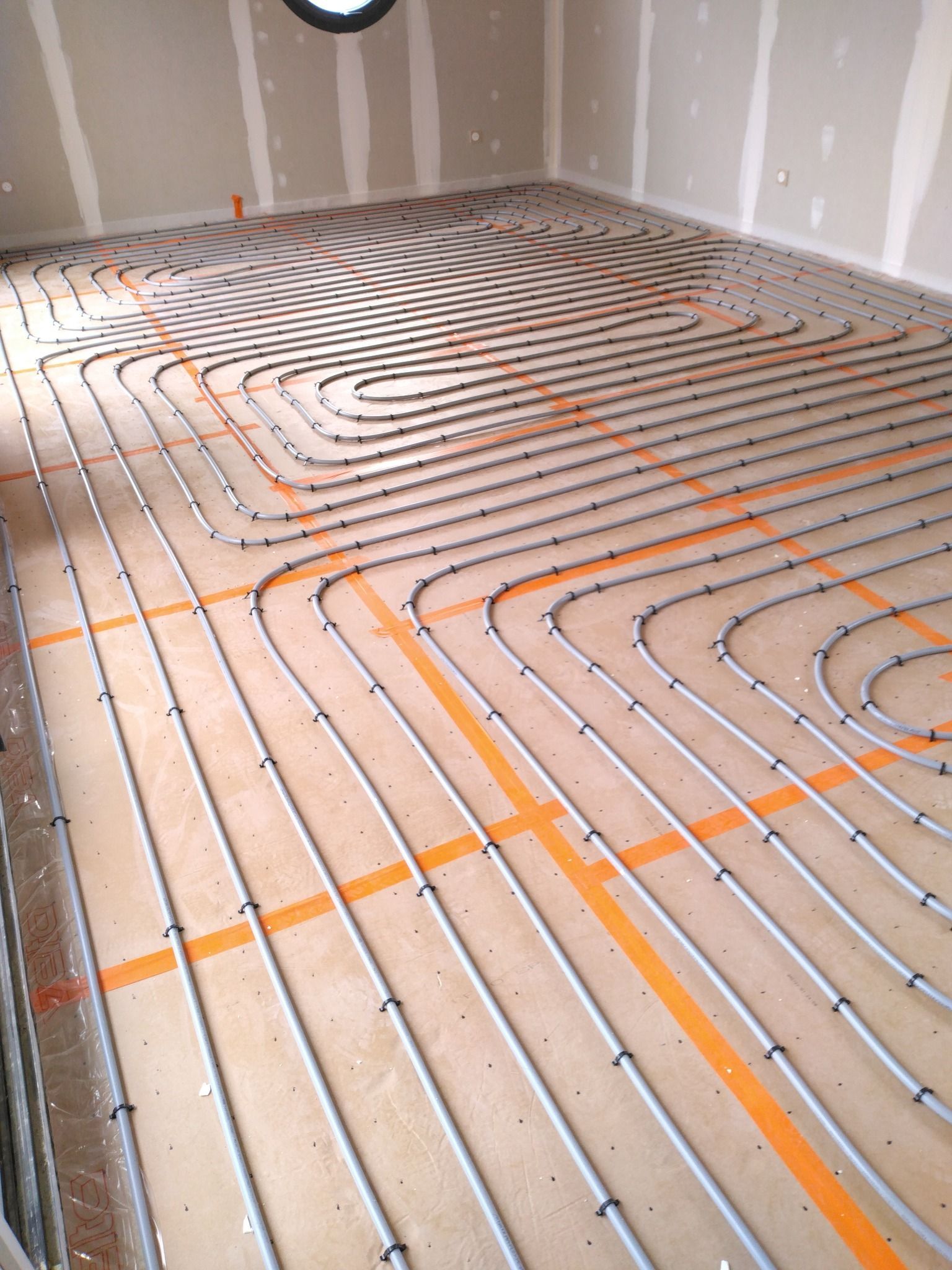 Installation d'un système de chauffage au sol avec des tuyaux gris et du ruban orange sur un sous-plancher.