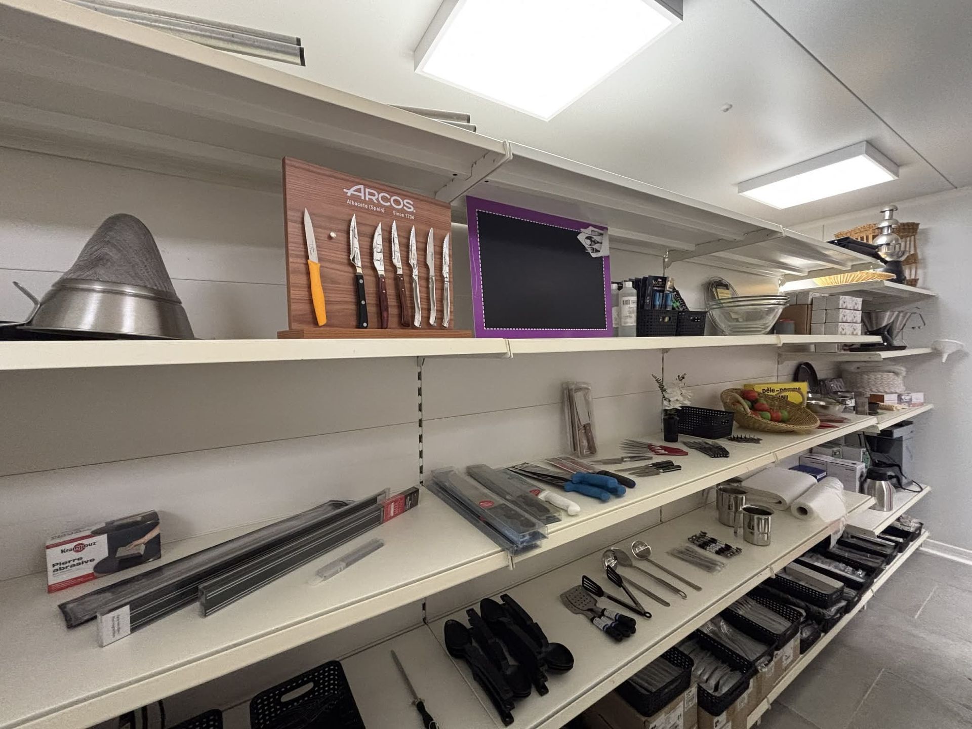 Des étagères remplies d'ustensiles de cuisine et de couteaux dans une pièce lumineuse.