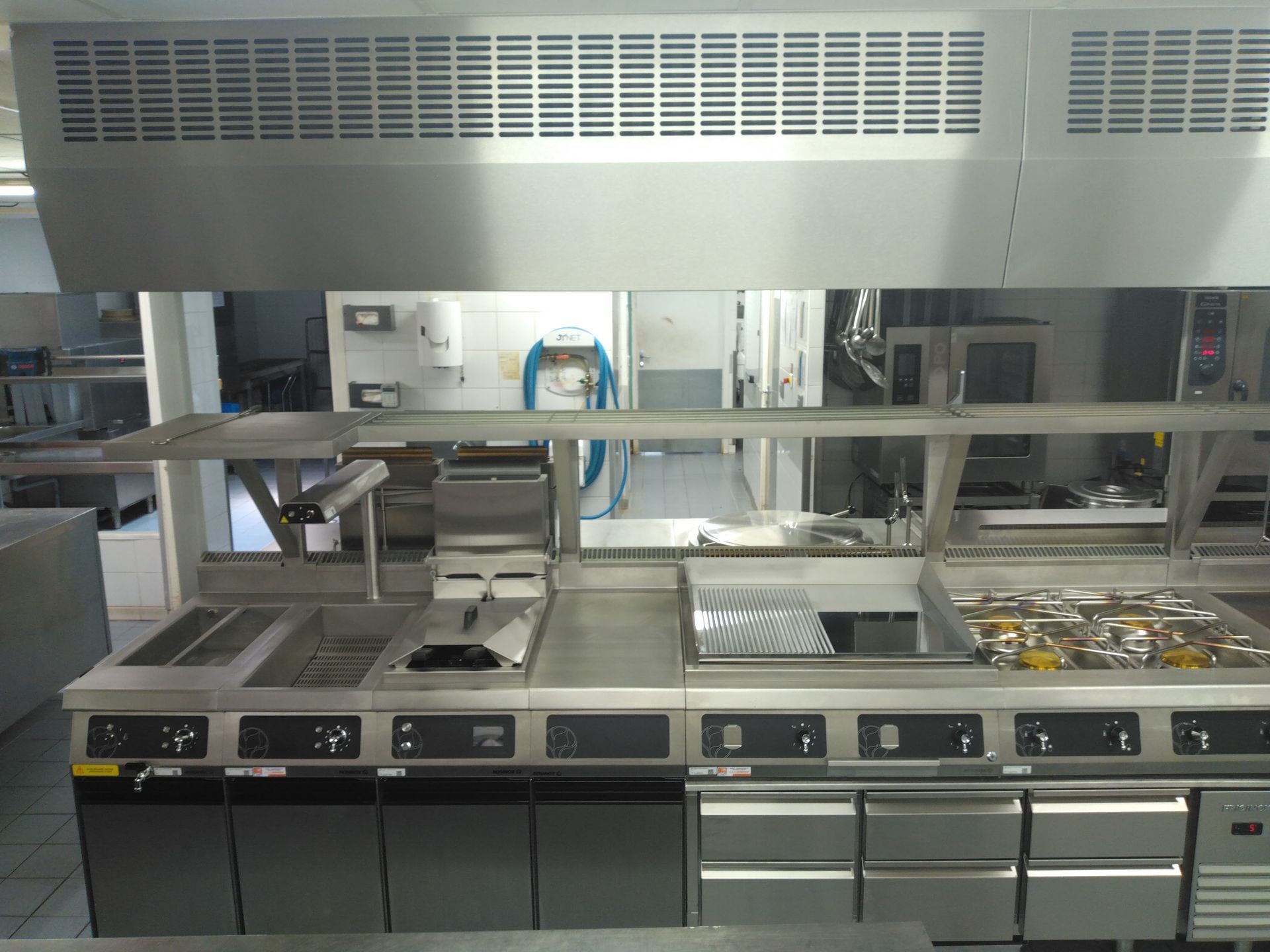 Cuisine professionnelle équipée d'appareils en acier inoxydable et d'une hotte aspirante.