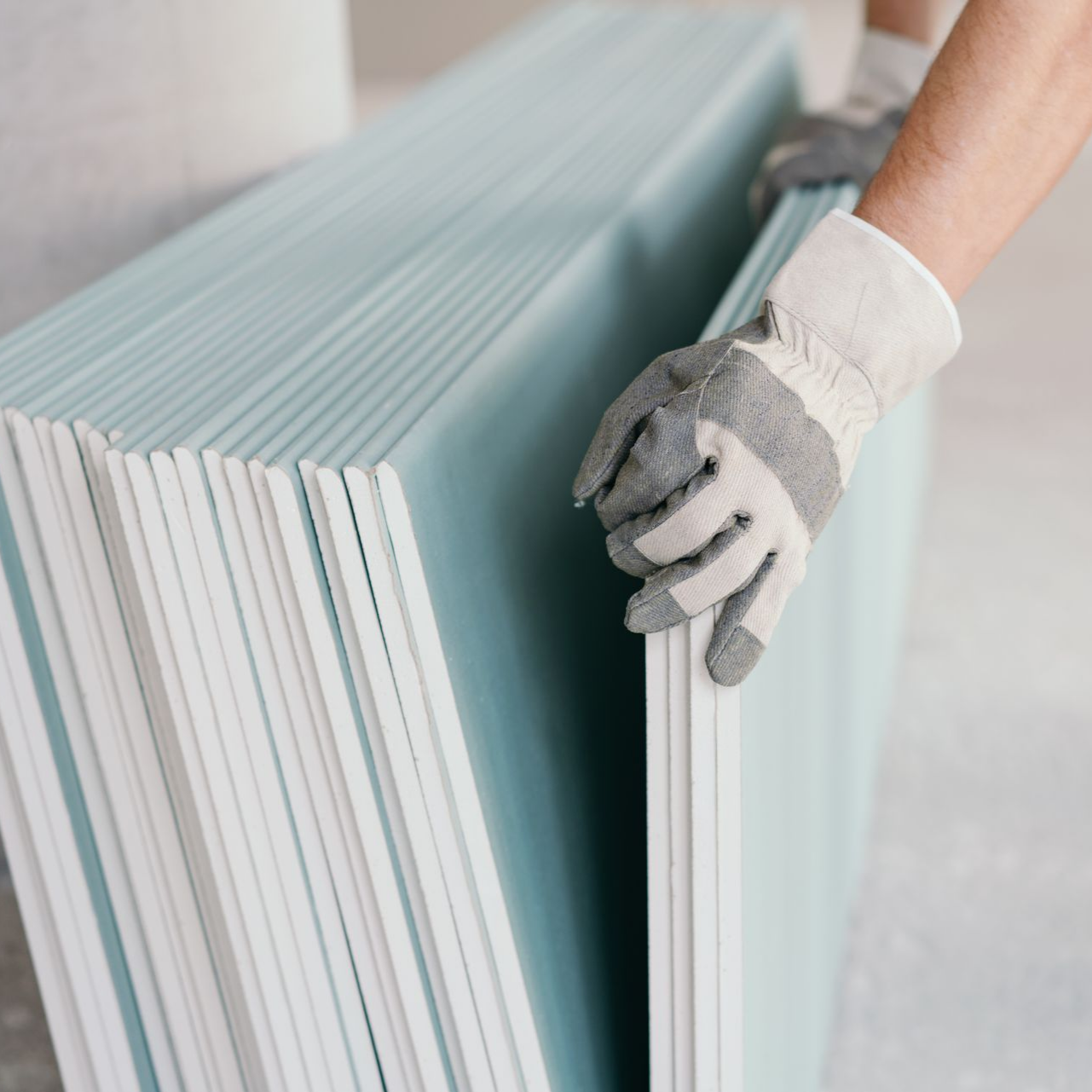 Main gantée empilant des panneaux de plaques de plâtre bleu clair.