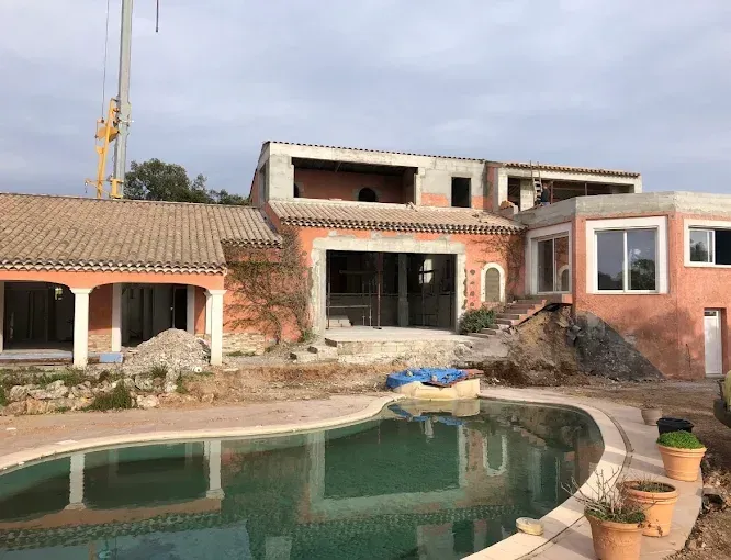 Maison en construction avec piscine à l'avant et grue en arrière-plan.