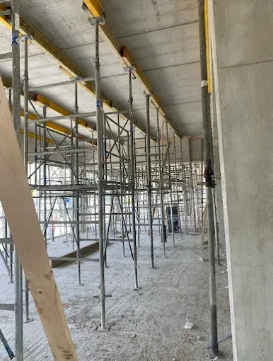 Chantier de construction intérieur avec échafaudages métalliques et colonnes de soutien sous un plafond en béton