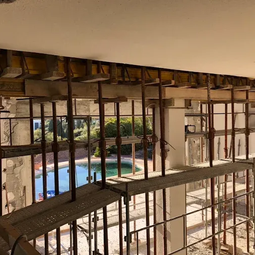 Intérieur d'un bâtiment partiellement démoli, avec charpente apparente, donnant sur une piscine.