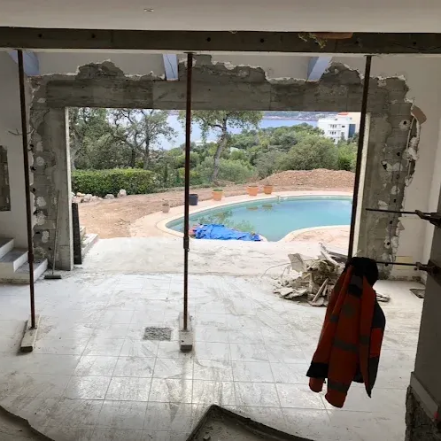 Pièce partiellement rénovée avec un mur ouvert donnant sur une terrasse et une piscine extérieure.