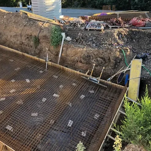 Chantier de construction avec treillis d'armature, remblai de terre excavée et canalisations.