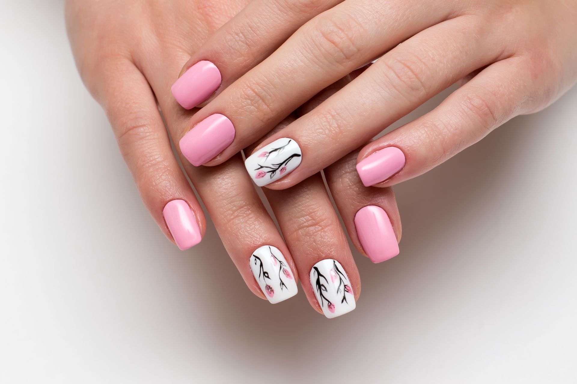 Hände mit manikürten Nägeln, die rosa und weiss lackiert sind und mit zarten schwarz-rosa floralen Zweigmotiven verziert sind.