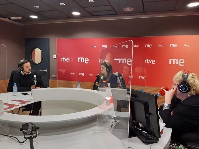 Un grupo de personas están sentadas frente a micrófonos en un estudio de radio.