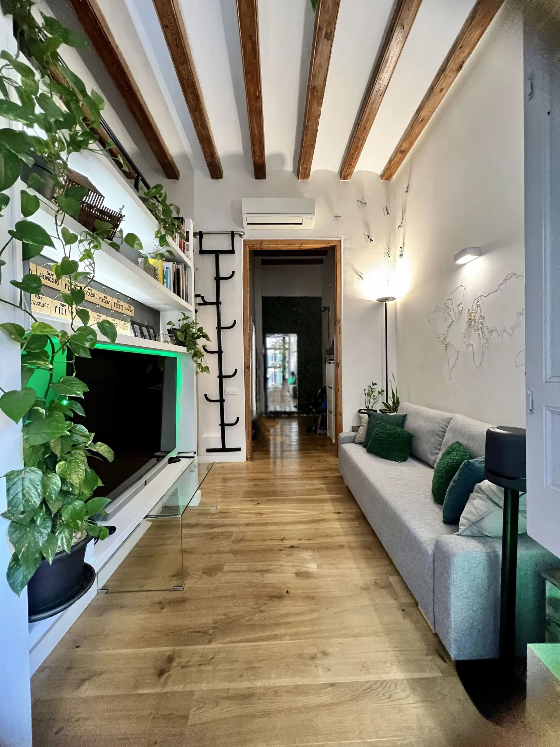 Una sala de estar con sofá, televisión y suelos de madera.
