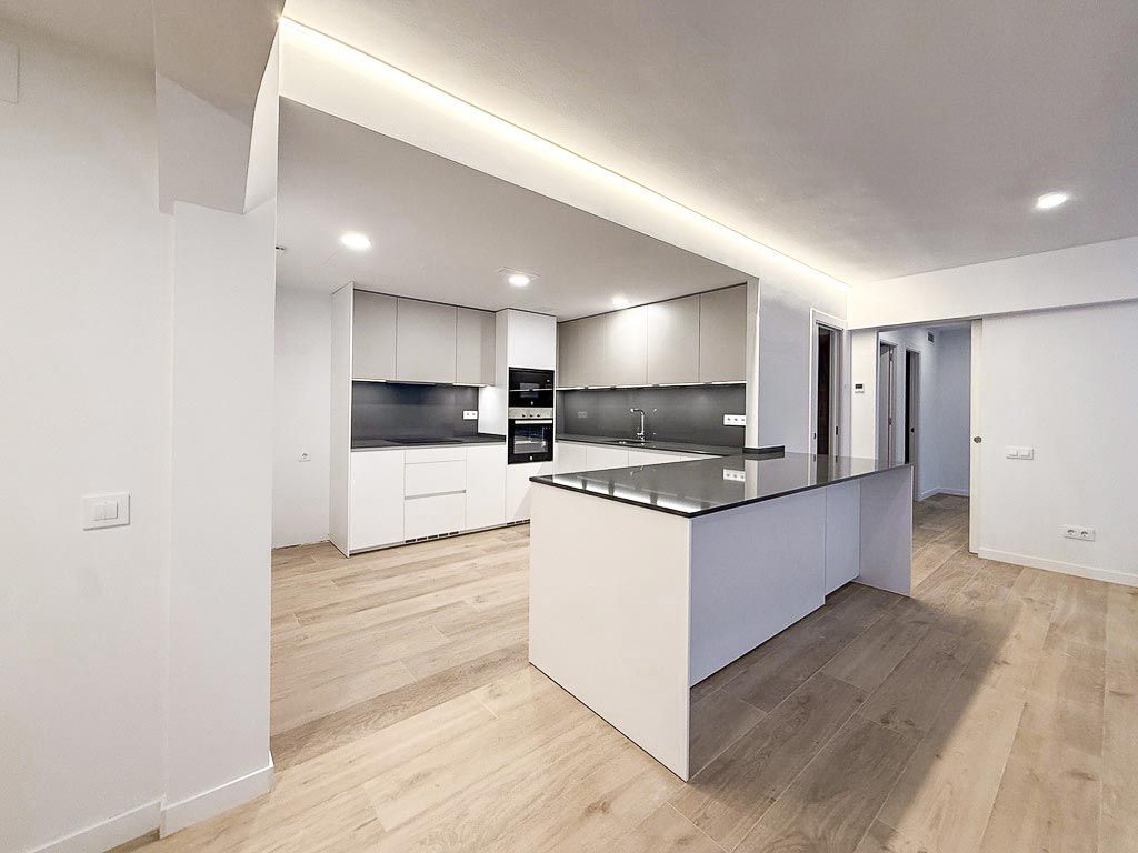 Cocina moderna con isla central, armarios blancos, encimeras grises y suelo de madera clara en una casa minimalista.