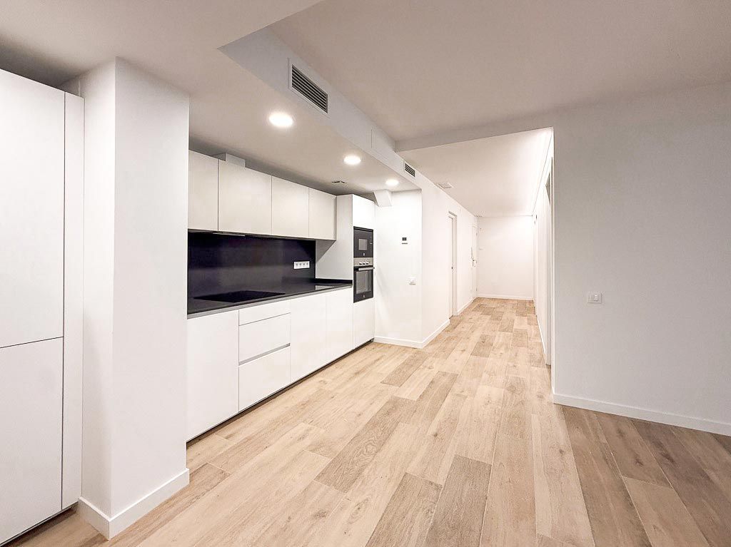 Cocina moderna con armarios blancos, encimeras oscuras y suelo de madera clara en un interior minimalista y luminoso.