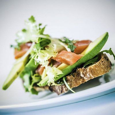 Un sándwich con aguacate, tomate y lechuga en un plato blanco.