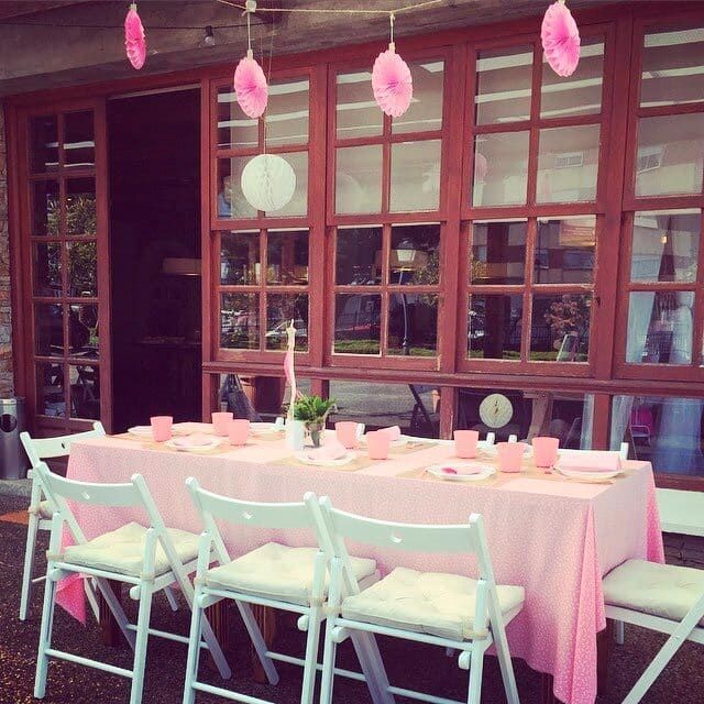 Una mesa con un mantel rosa y sillas blancas.