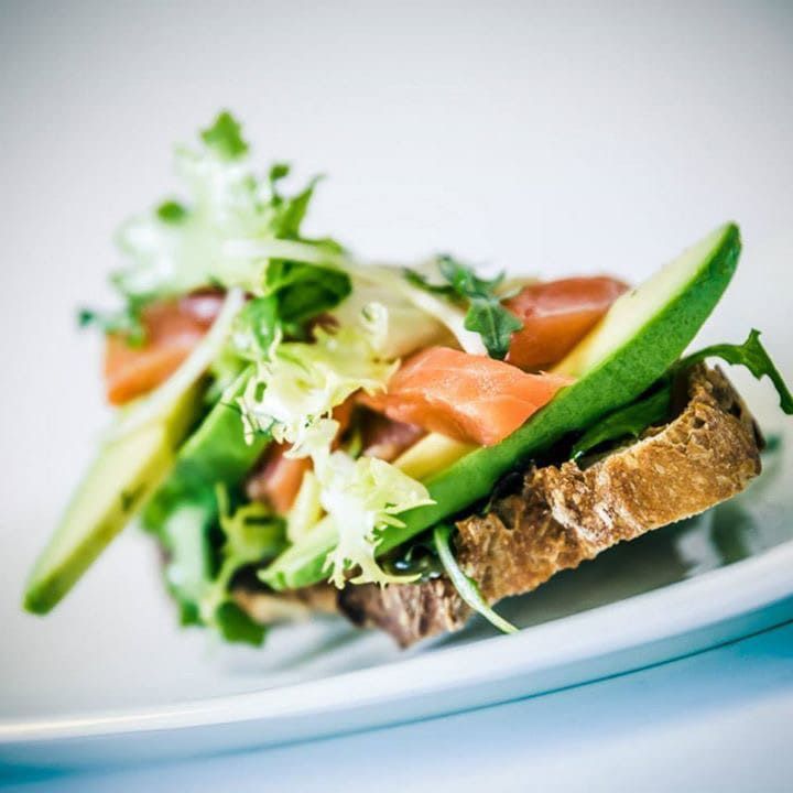 Un sándwich con lechuga, tomate y aguacate en un plato blanco.