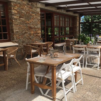 Mesas y sillas en el exterior de un restaurante con un muro de piedra.