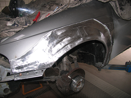 Ein Auto mit einem beschädigten Kotflügel steht auf einer Hebebühne in einer Garage.