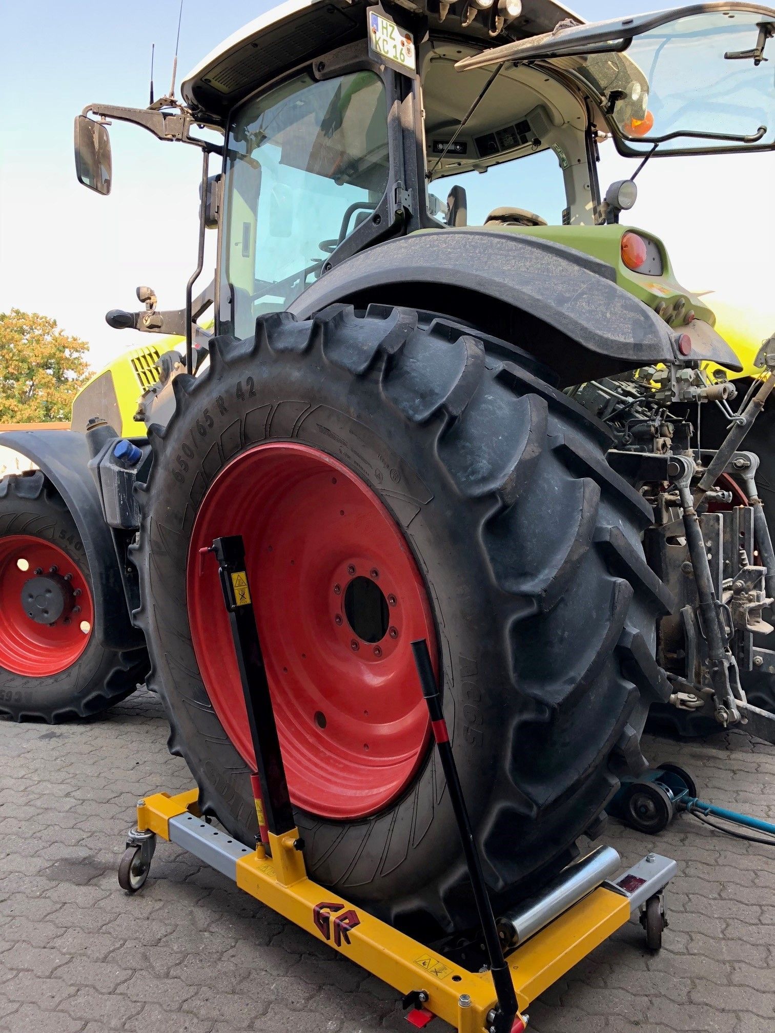 Auf einem gelben Wagen steht ein Traktor mit einem roten Reifen.