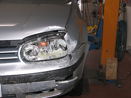 Ein silbernes Auto mit einem beschädigten Scheinwerfer steht in einer Garage.
