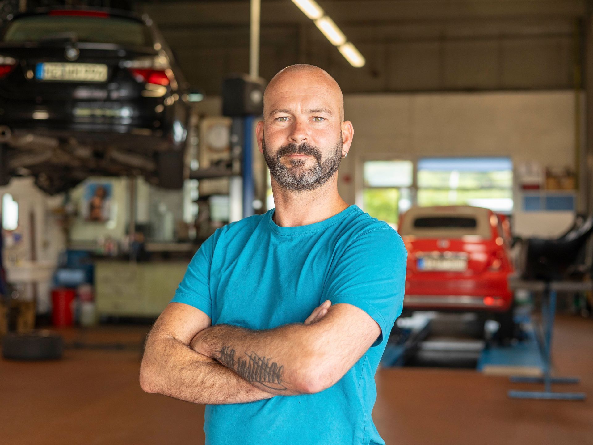 Ein Mann mit Bart steht mit verschränkten Armen in einer Garage.