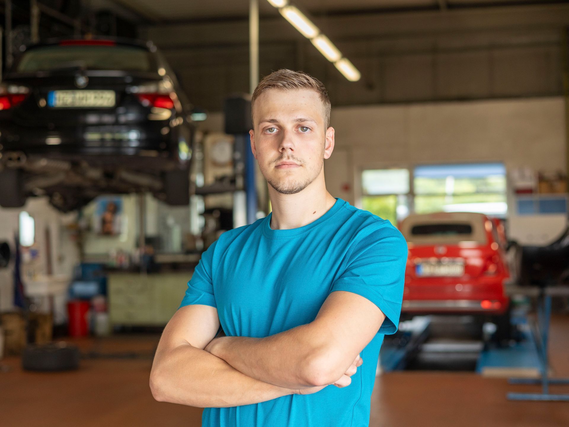 Ein Mann in einem blauen Hemd steht mit verschränkten Armen in einer Garage.
