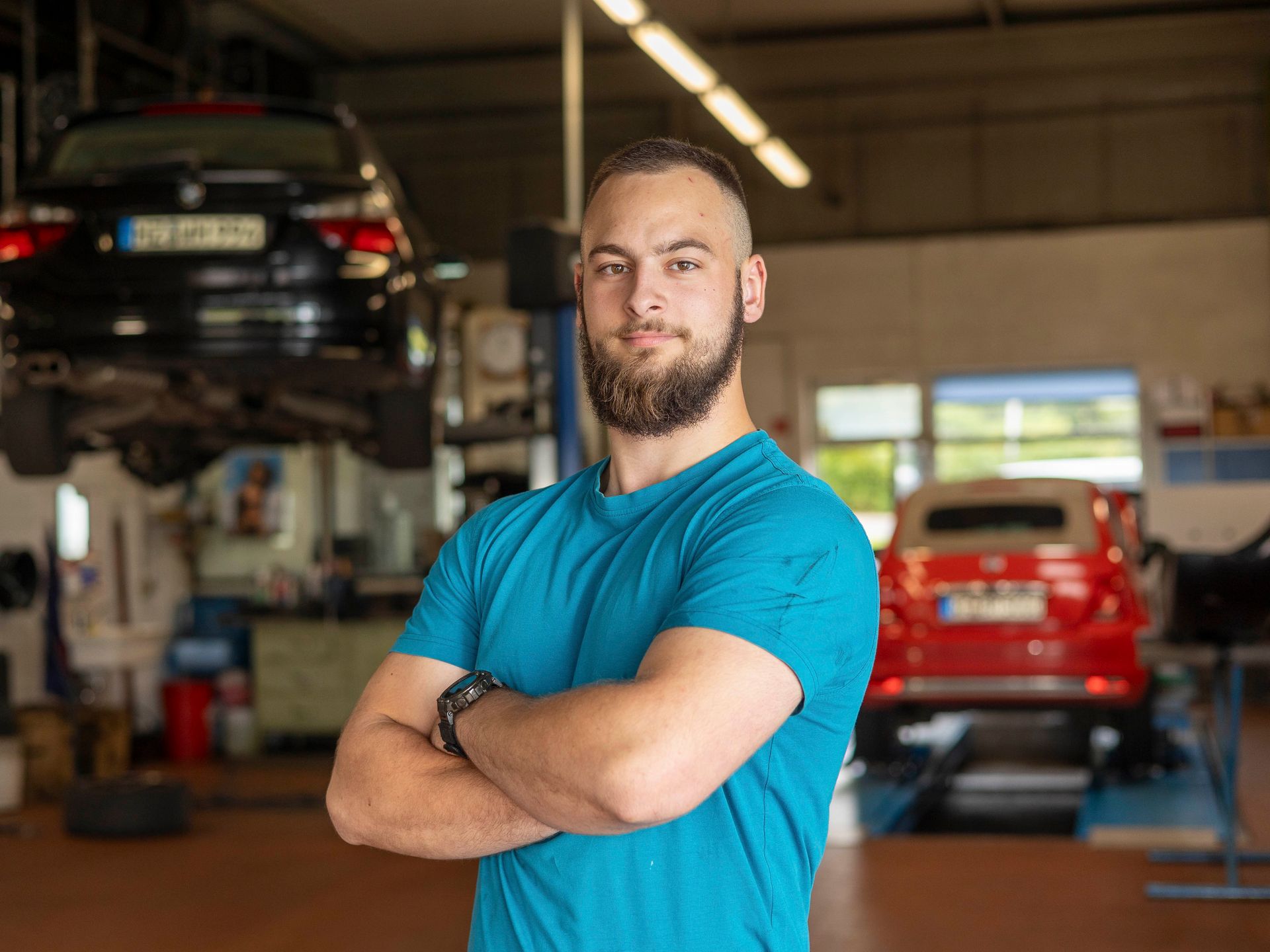 Ein Mann in einem blauen Hemd steht mit verschränkten Armen in einer Garage.