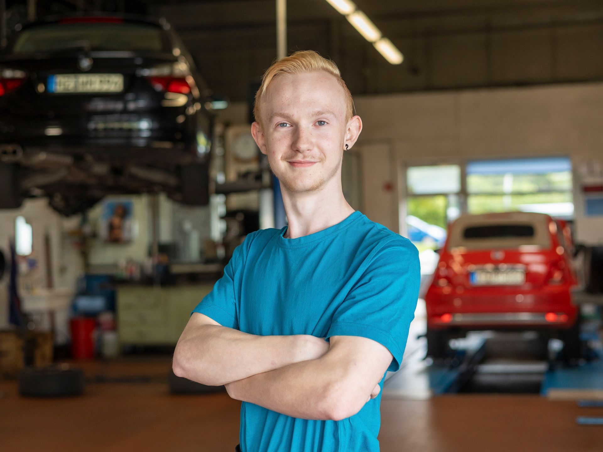 Ein Mann in einem blauen Hemd steht mit verschränkten Armen in einer Garage.