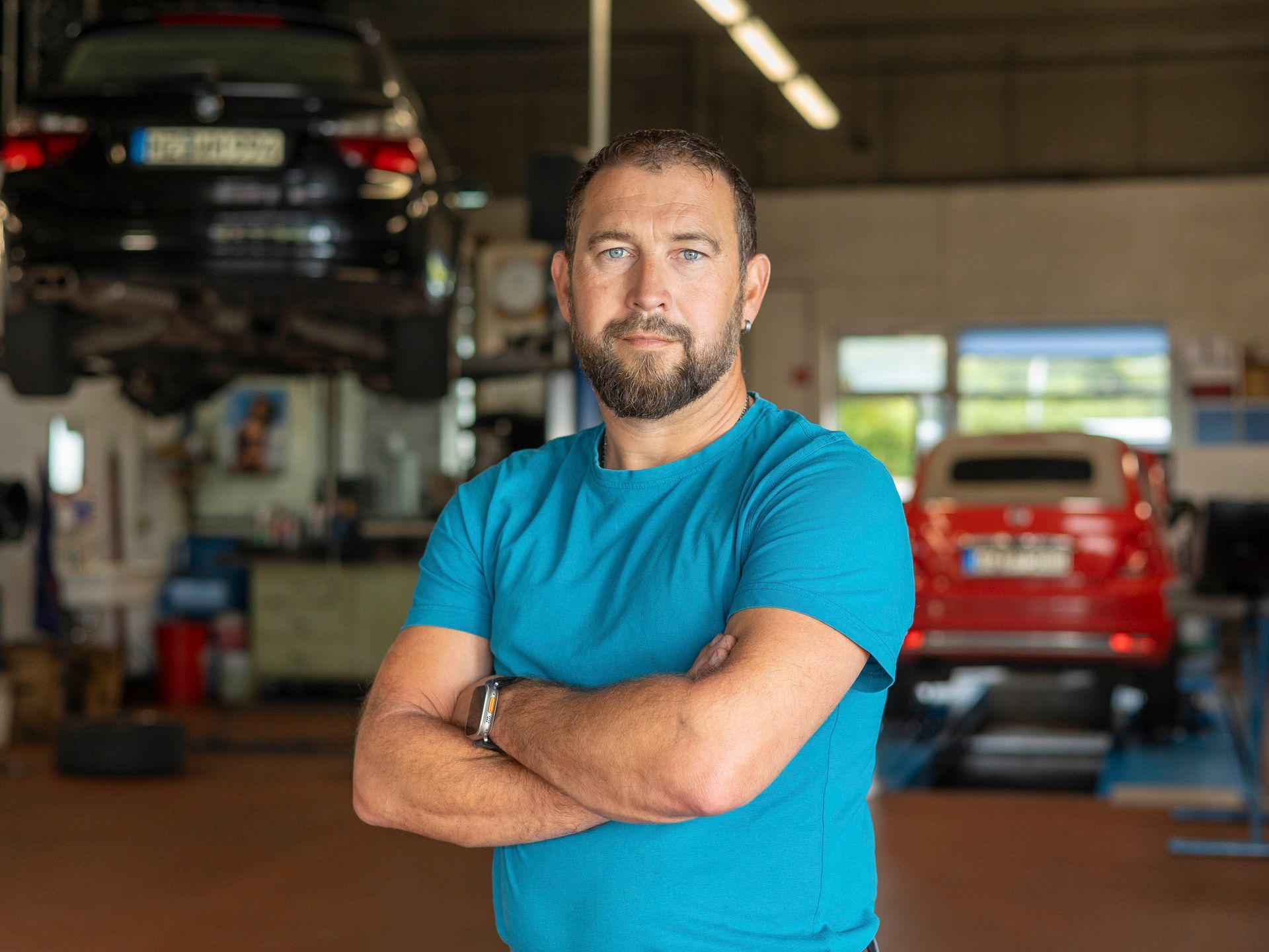 Ein Mann in einem blauen Hemd steht mit verschränkten Armen in einer Garage.