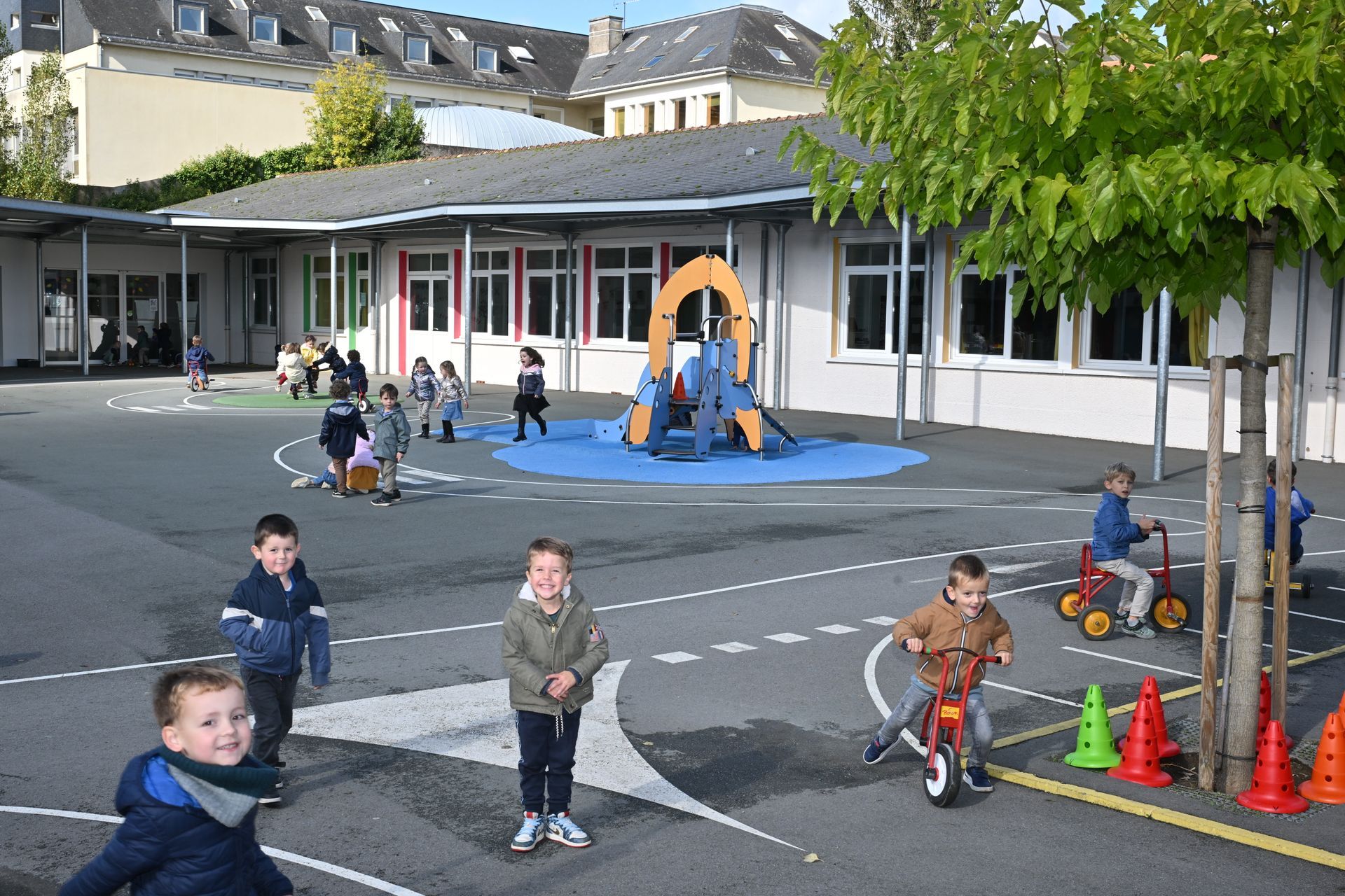 Cour d’école avec des enfants qui  jouent sur des tricycles, près d’une structure de jeu bleue et jaune