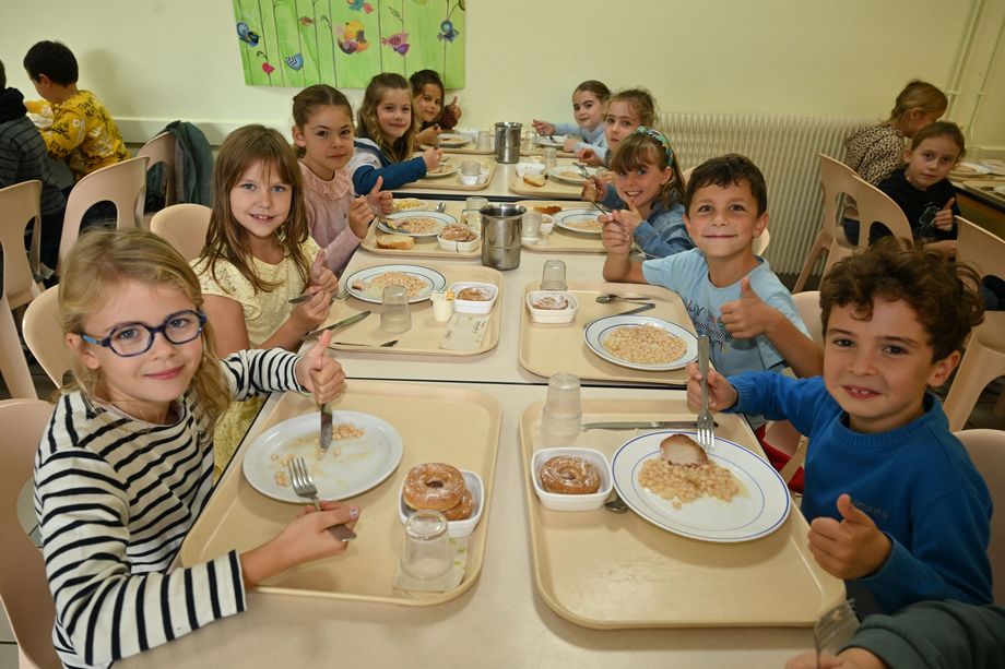 Groupe d’enfants assis à une table dans une cantine, mangeant un repas avec des plateaux et des assiettes