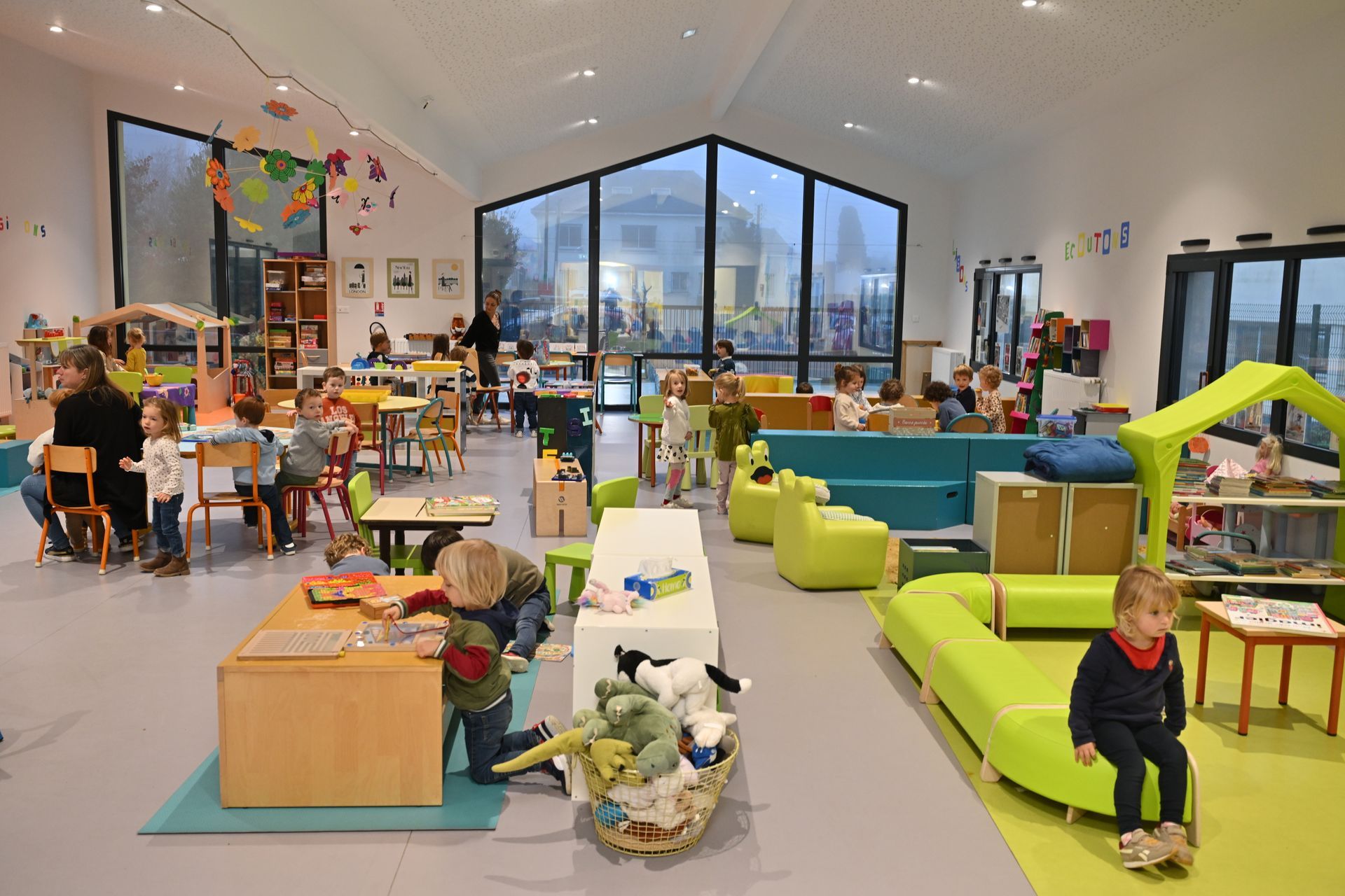 Salle lumineuse d’accueil pour enfants avec plusieurs espaces de jeux, tables d’activités, jouets et mobilier coloré
