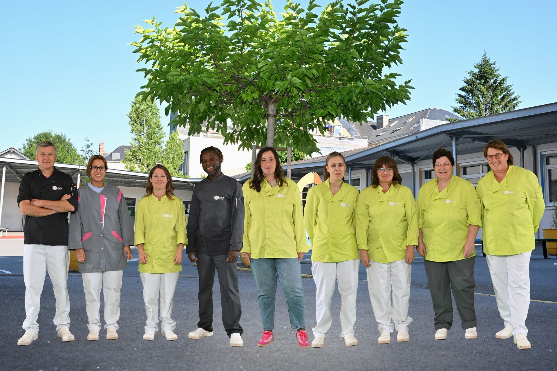 Groupe de personnes debout en extérieur, alignées devant un arbre portant des uniformes composés de hauts verts