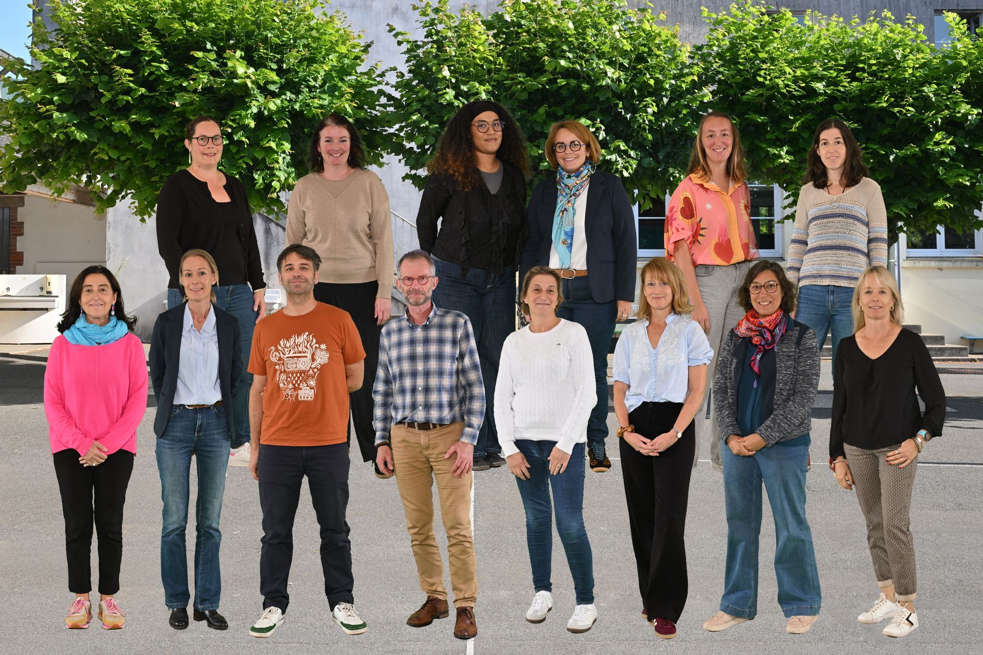 Groupe d’adultes debout en extérieur, disposés en deux rangées devant un arbre verdoyant