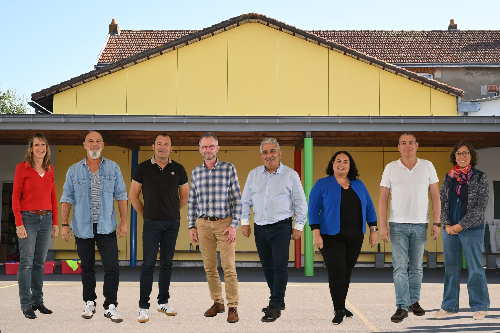 Groupe d’adultes debout devant un bâtiment scolaire à façade jaune avec toit en tuiles