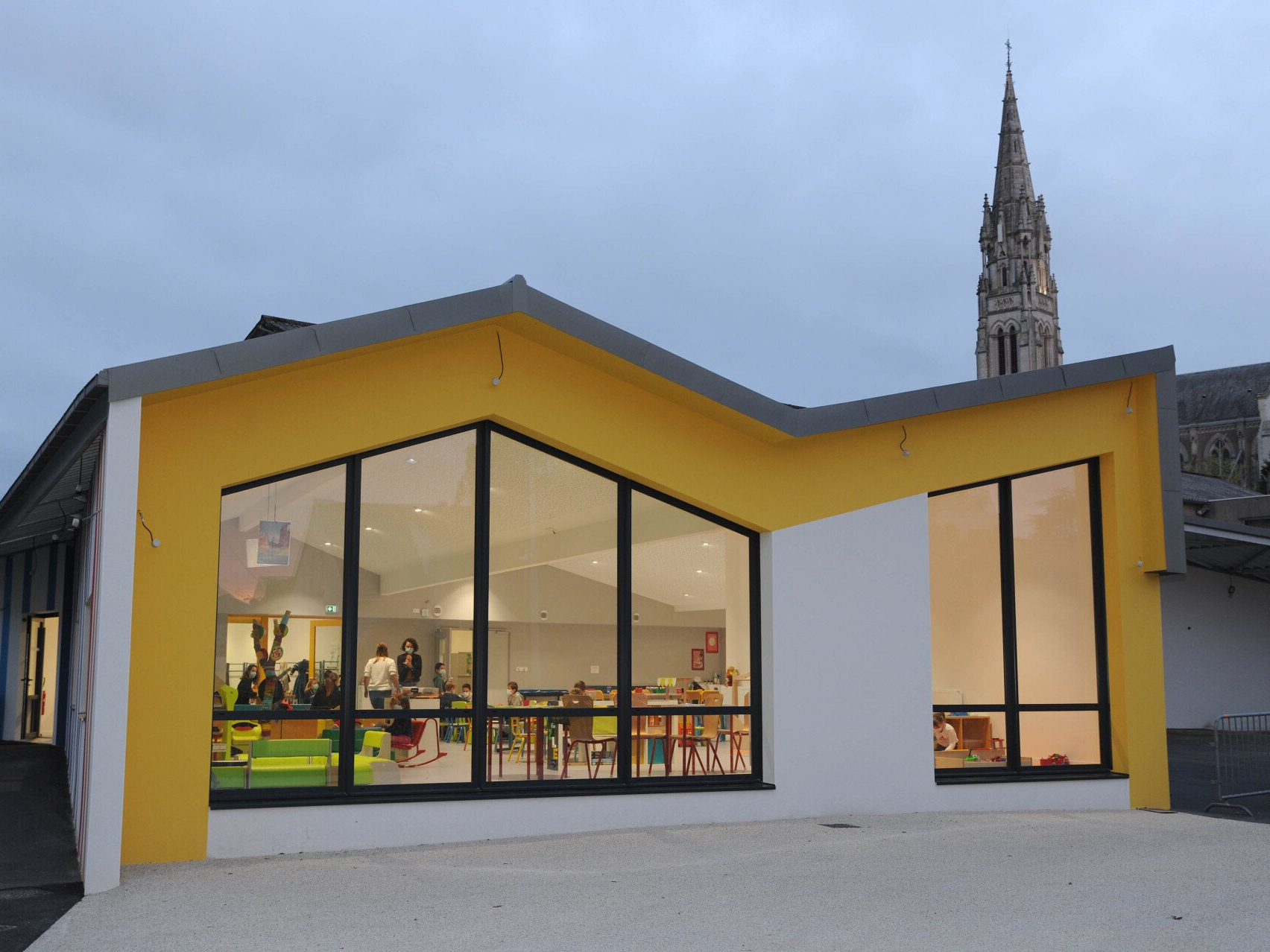 Vue extérieure d’un bâtiment moderne avec une façade blanche et un encadrement jaune vif autour de grandes baies vitrées.