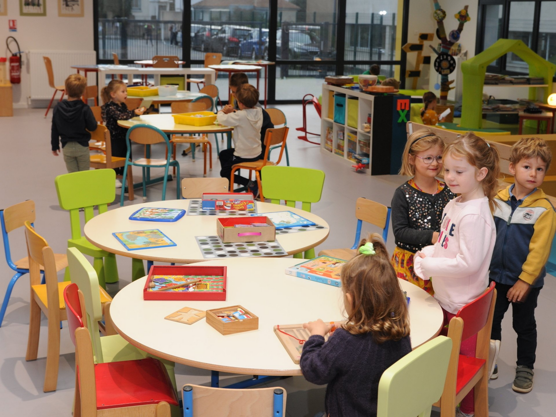 Salle de jeux lumineuse avec plusieurs tables rondes et chaises colorées avec des enfants