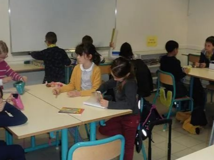 Salle de classe avec plusieurs élèves assis autour de tables, travaillant sur des cahiers