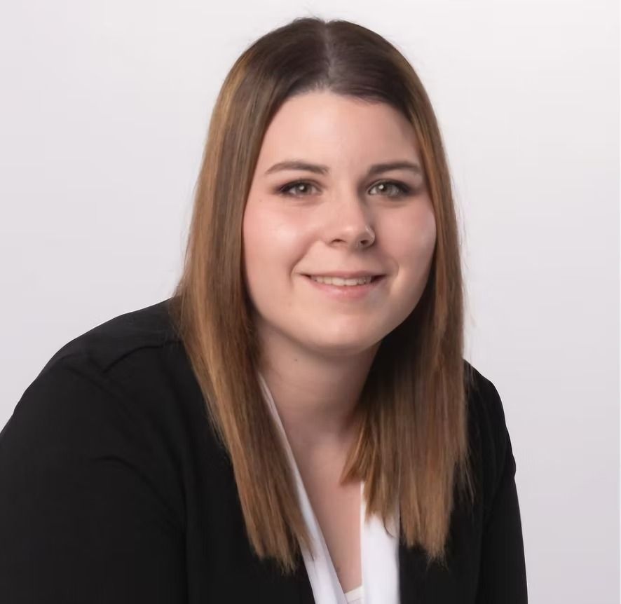 Eine Frau mit hellbraunem Haar lächelt. Sie trägt einen schwarzen Blazer und ein weisses Oberteil.