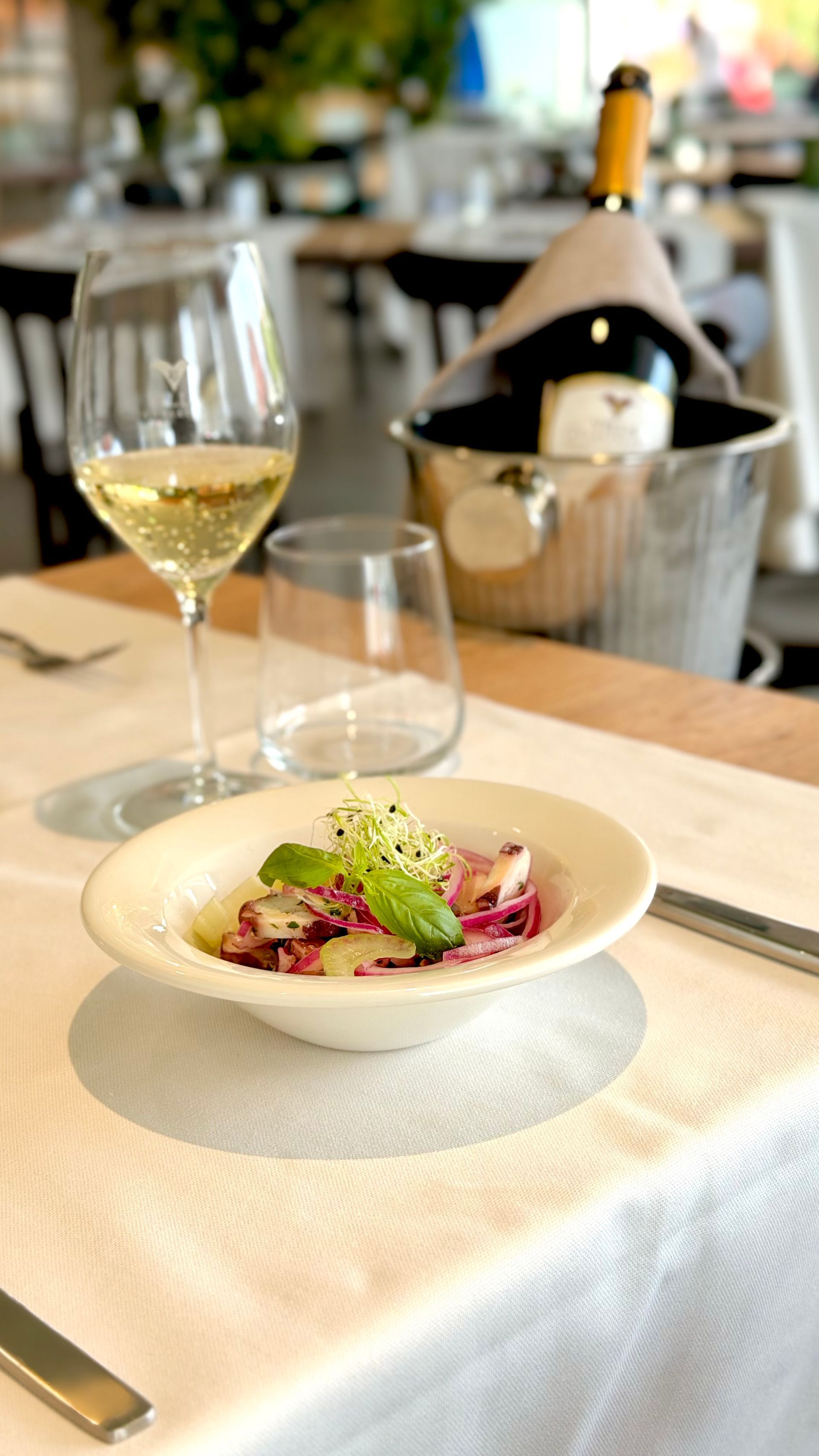 Persone che mangiano spaghetti a un tavolo con calici di vino, in un ambiente accogliente e con luci soffuse.