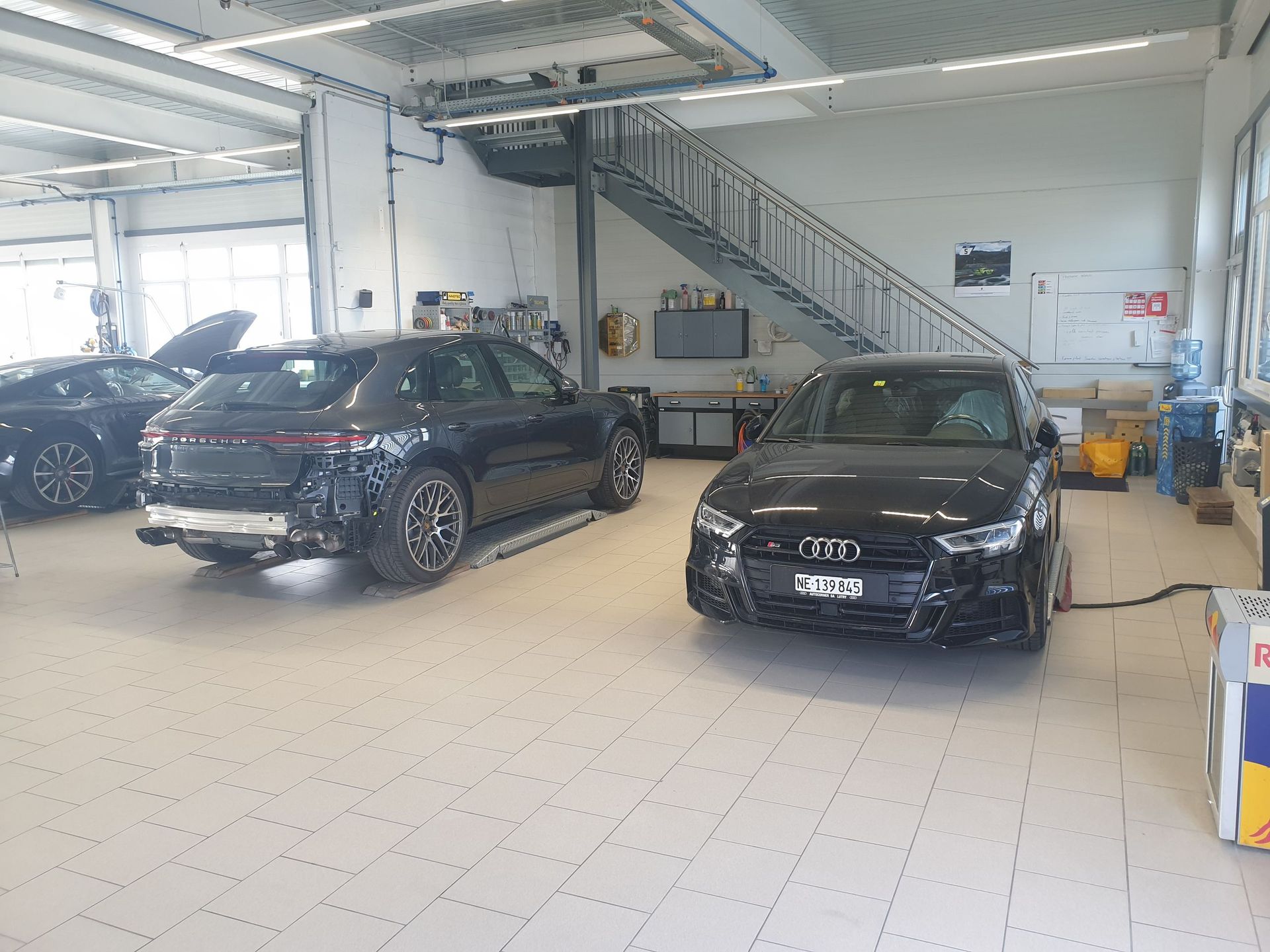 Deux voitures noires sont garées dans un garage avec des escaliers.