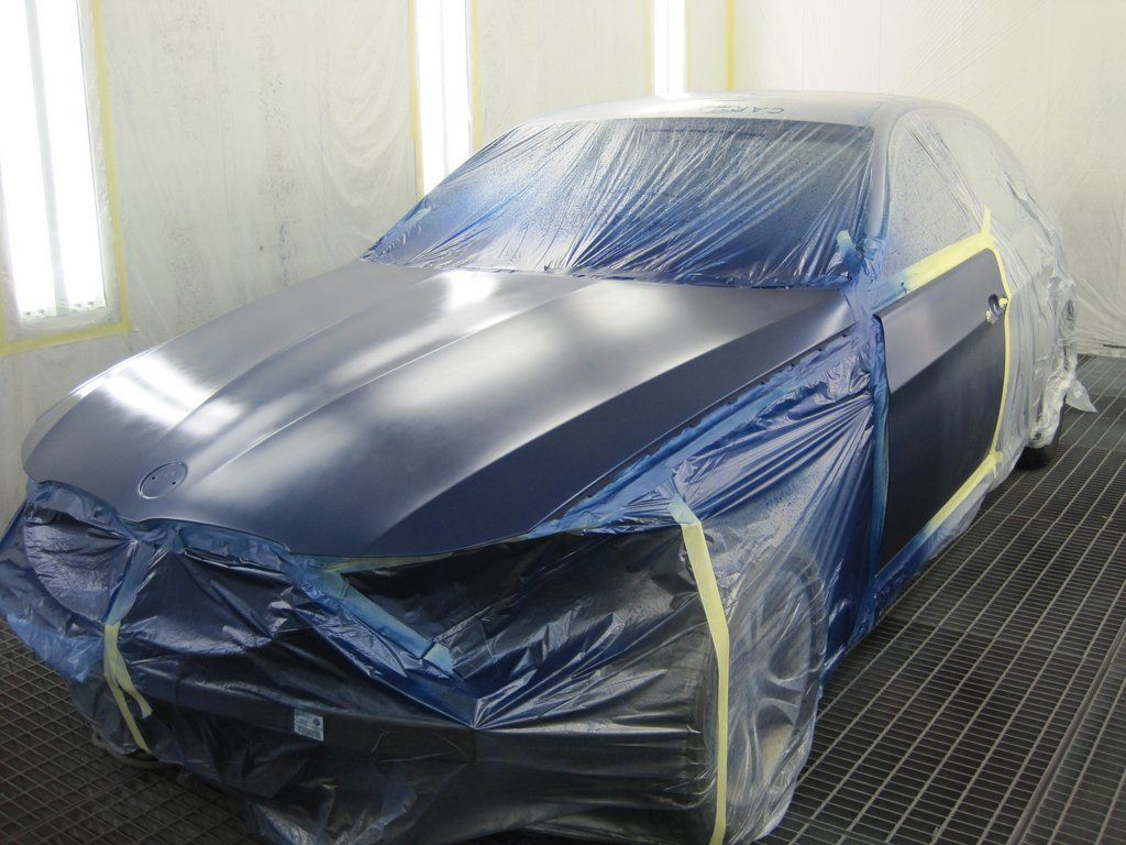 Une voiture est recouverte de plastique dans une cabine de peinture.