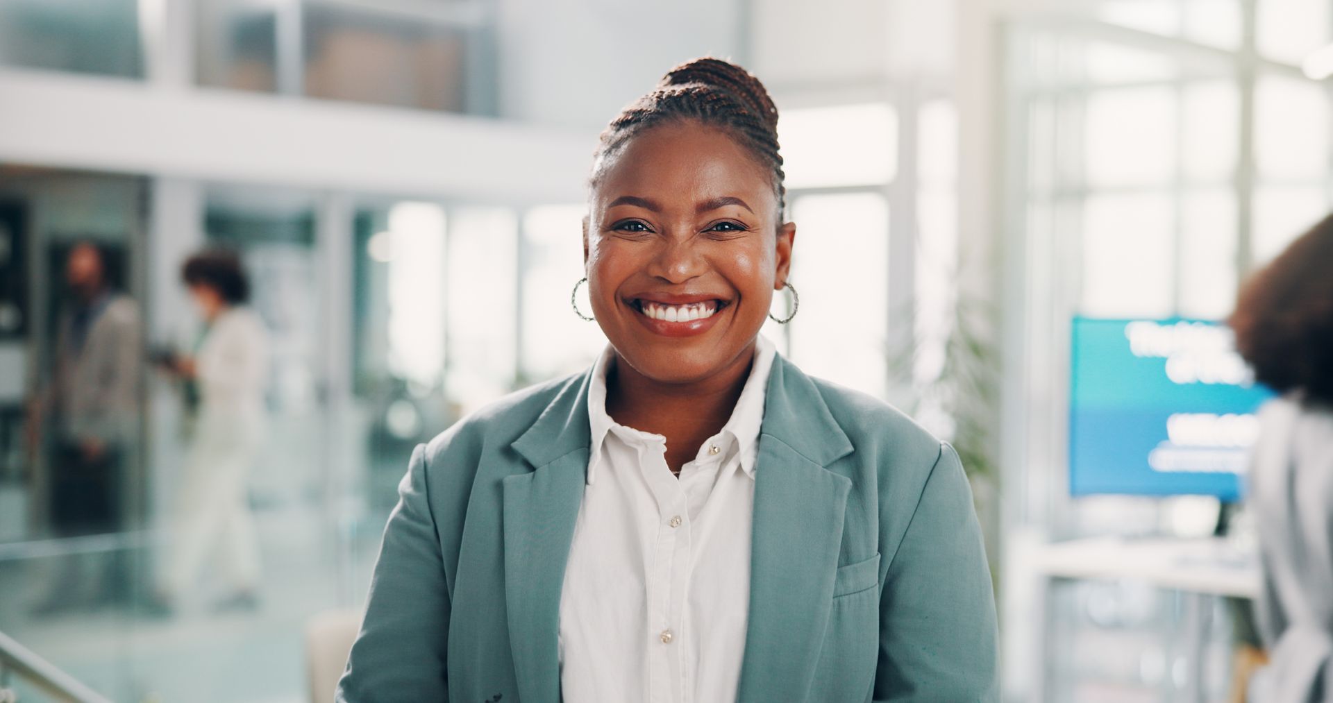 Une femme souriante, vêtue d'un blazer clair, se tient dans le hall lumineux d'un immeuble de bureaux.