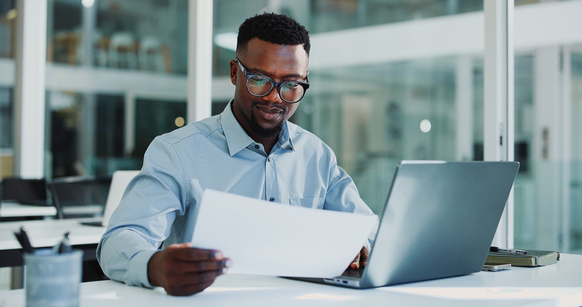 Une personne examine des documents à côté d'un ordinateur portable dans un bureau lumineux.