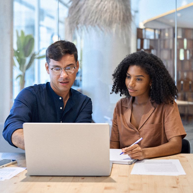 Deux collègues examinent des documents à côté d'un ordinateur portable dans un bureau lumineux.