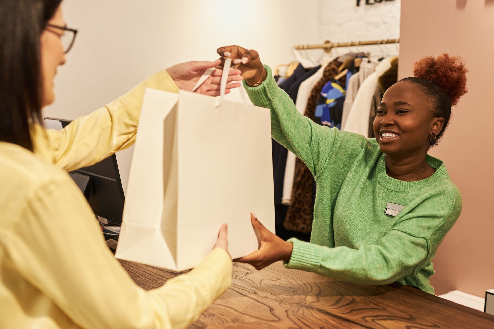 Deux personnes dans un magasin de vêtements tiennent ensemble un sac de courses couleur crème et sourient.