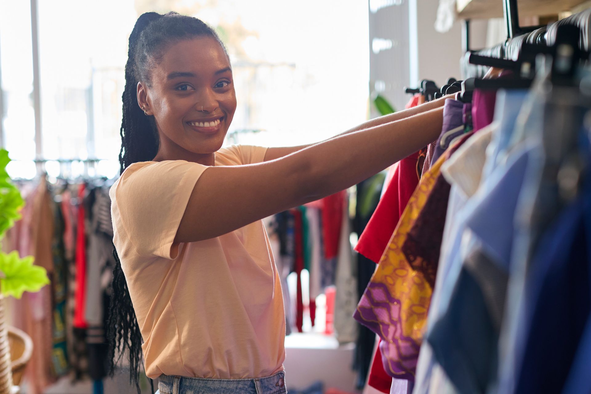 Une femme sourit en regardant des vêtements sur des portants dans un magasin de vêtements.