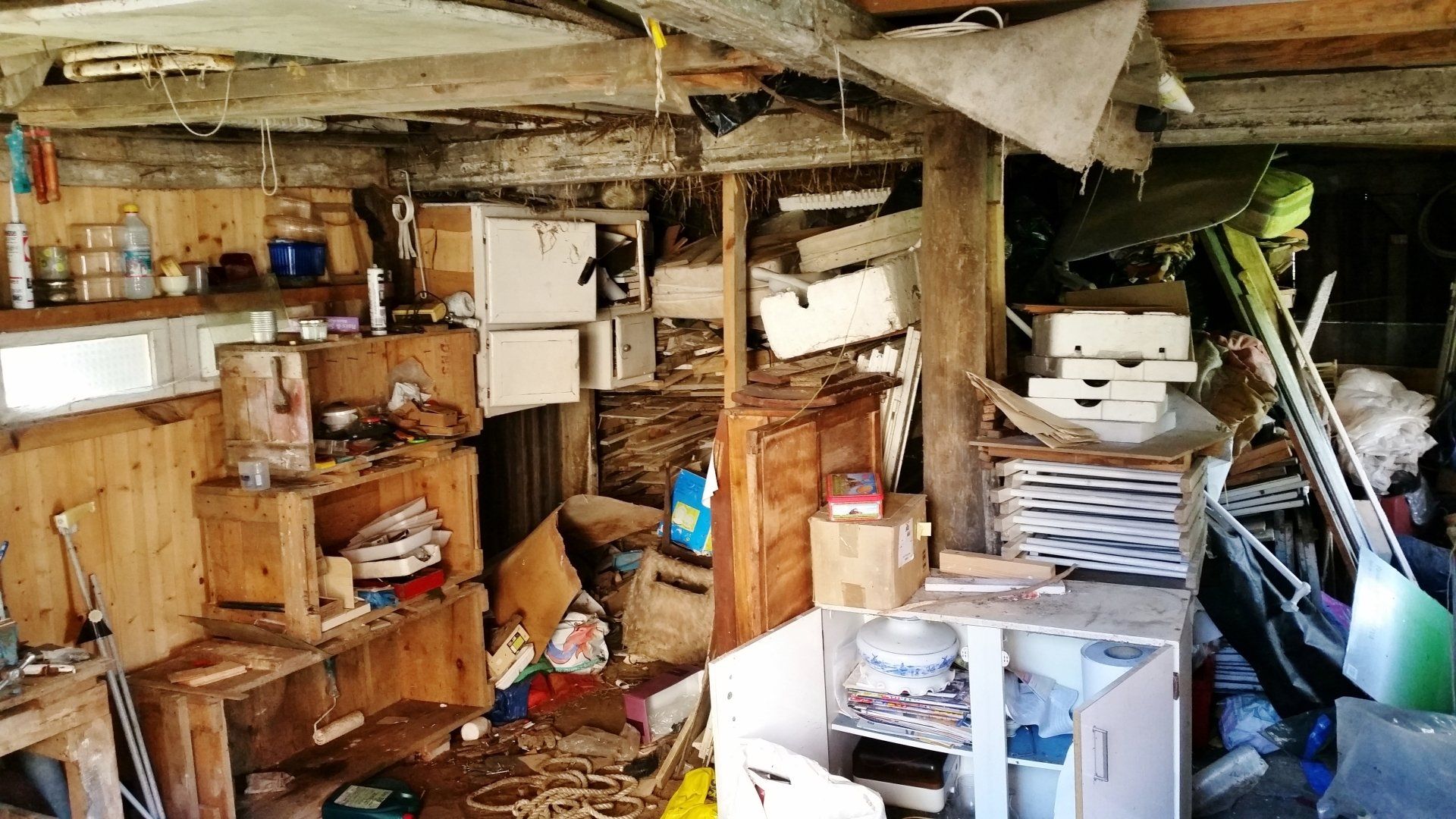 Espace de rangement encombré d'étagères en bois, de boîtes et d'objets divers. L'intérieur est désordonné.