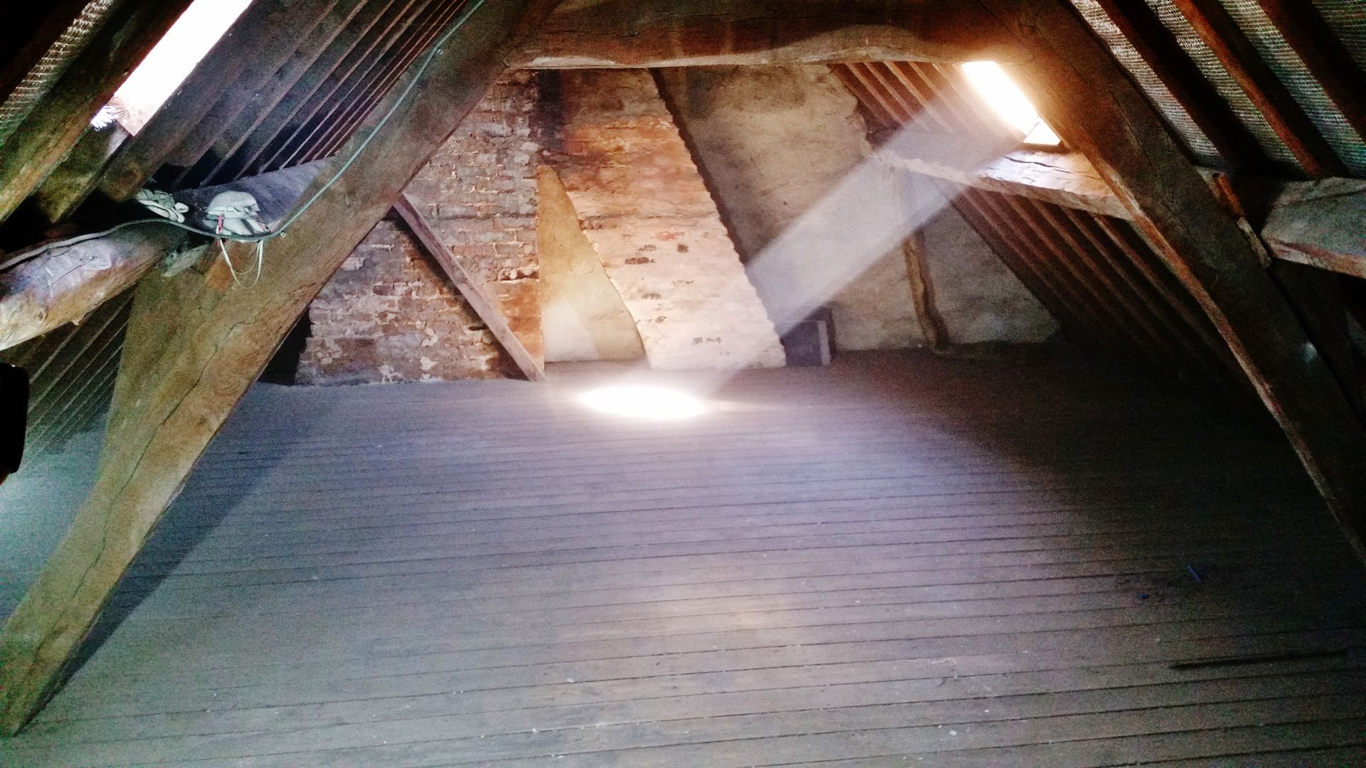 La lumière du soleil filtre à travers un grenier poussiéreux, illuminant les poutres en bois et un sol sombre.