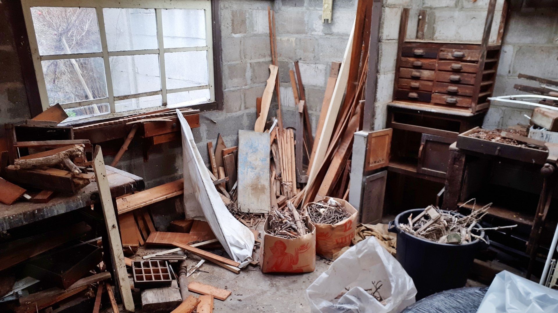 Un atelier encombré de matériaux, mobilier et déchets.