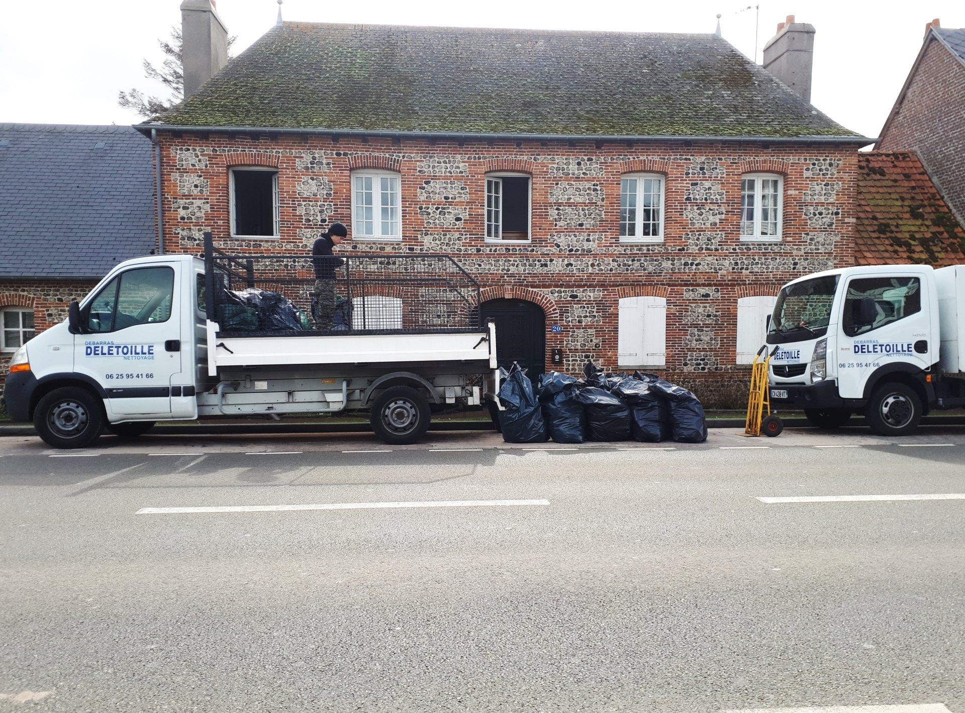 Des sacs-poubelle entre 2 camions-bennes devant une maison.