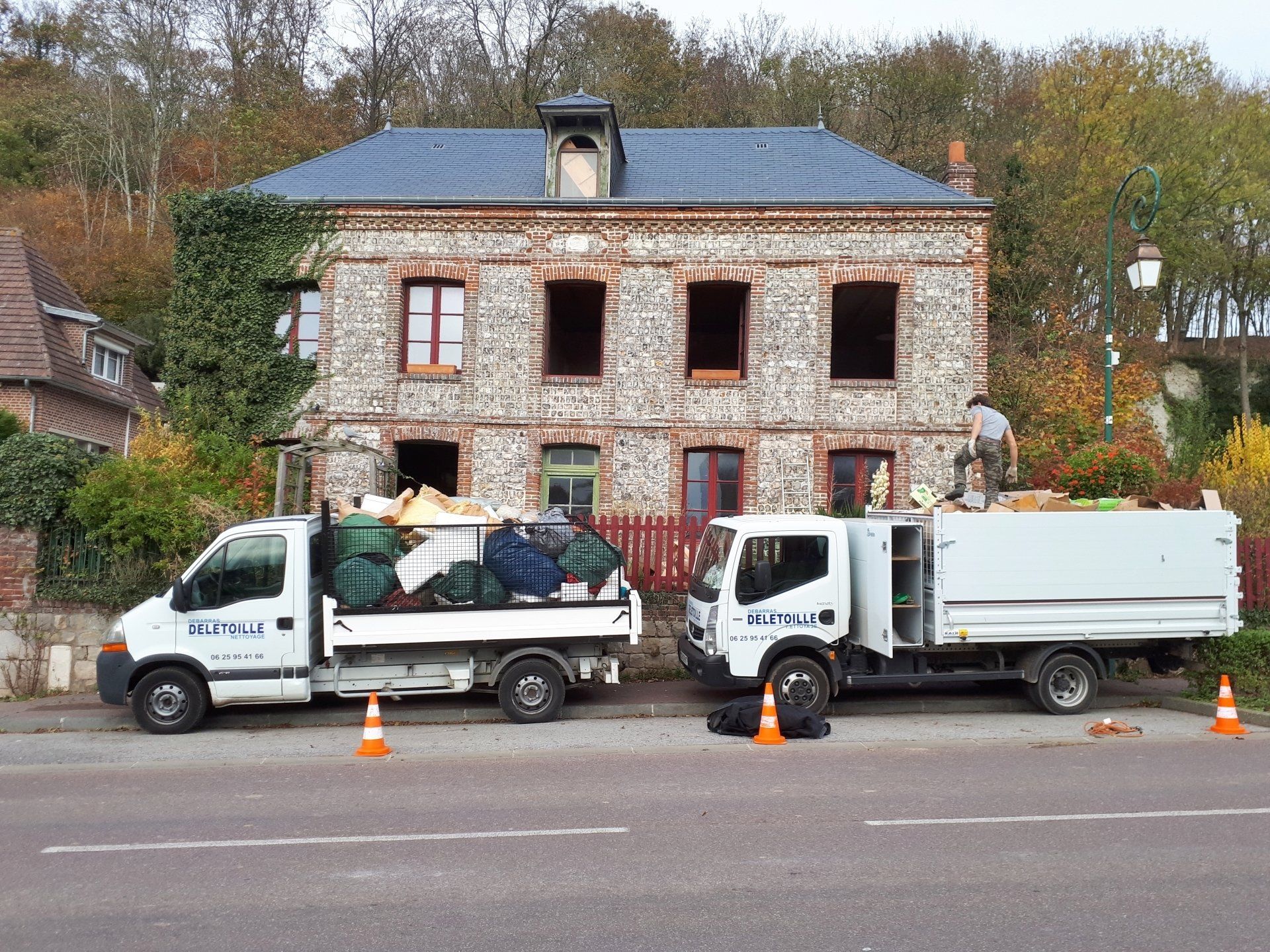 Camions de débarras stationnés devant une maison aux fenêtres ouvertes.